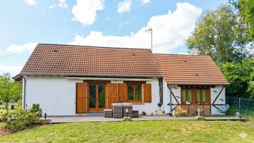 A single-story house with a tiled roof, a front porch with outdoor furniture, and a small garden area.