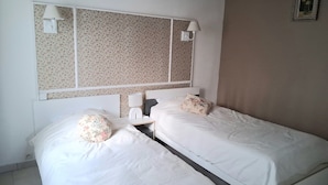 Ein Hotelzimmer mit zwei Einzelbetten, einem großen Spiegel darüber, einem Nachttisch mit Lampe und einem Wandbild.