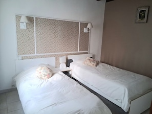 Ett hotellrum med två separata sängar, en stor spegel ovanför sängarna, ett nattduksbord med en lampa och en tavla som hänger på väggen.