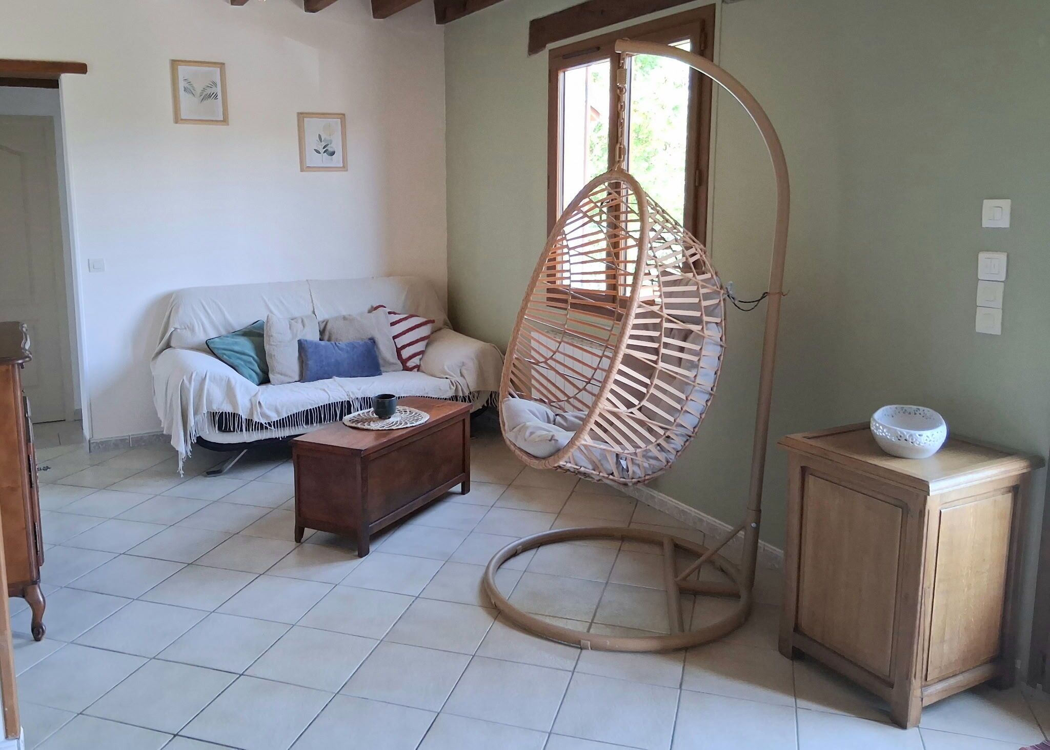 Una sala de estar con sofá, una silla colgante, un aparador de madera y piso de baldosas.