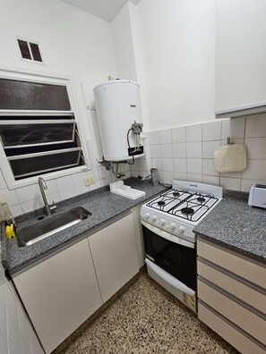 Een kleine keuken met een spoelbak, fornuis en een boiler.