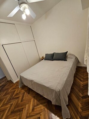 Een slaapkamer met een bed, een plafondventilator en een kledingkast.