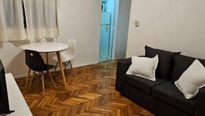 A living room with a ceiling fan, a black sofa, a white table with chairs, and a herringbone wooden floor. - Comfortable and Well-Located in Recoleta (Buenos Aires)