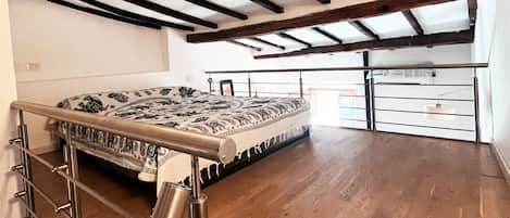 A room with a wooden floor, a bed with patterned bedding, and a metal railing.
