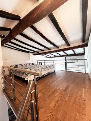 A room with a wooden floor, a bed with patterned bedding, and a metal railing. - Il Nido di Marciana (Marciana)