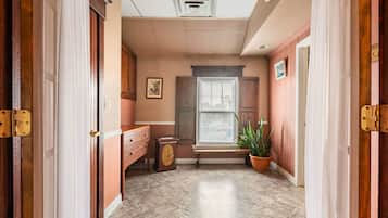 A hallway with a bench, a window with blinds, a potted plant, and a door with a latch.