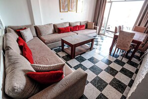 A living room with a sectional sofa, a coffee table, and a dining area with chairs and a table. - Charming 2-bedroom Apartment With Direct sea View in Martil (Martil)