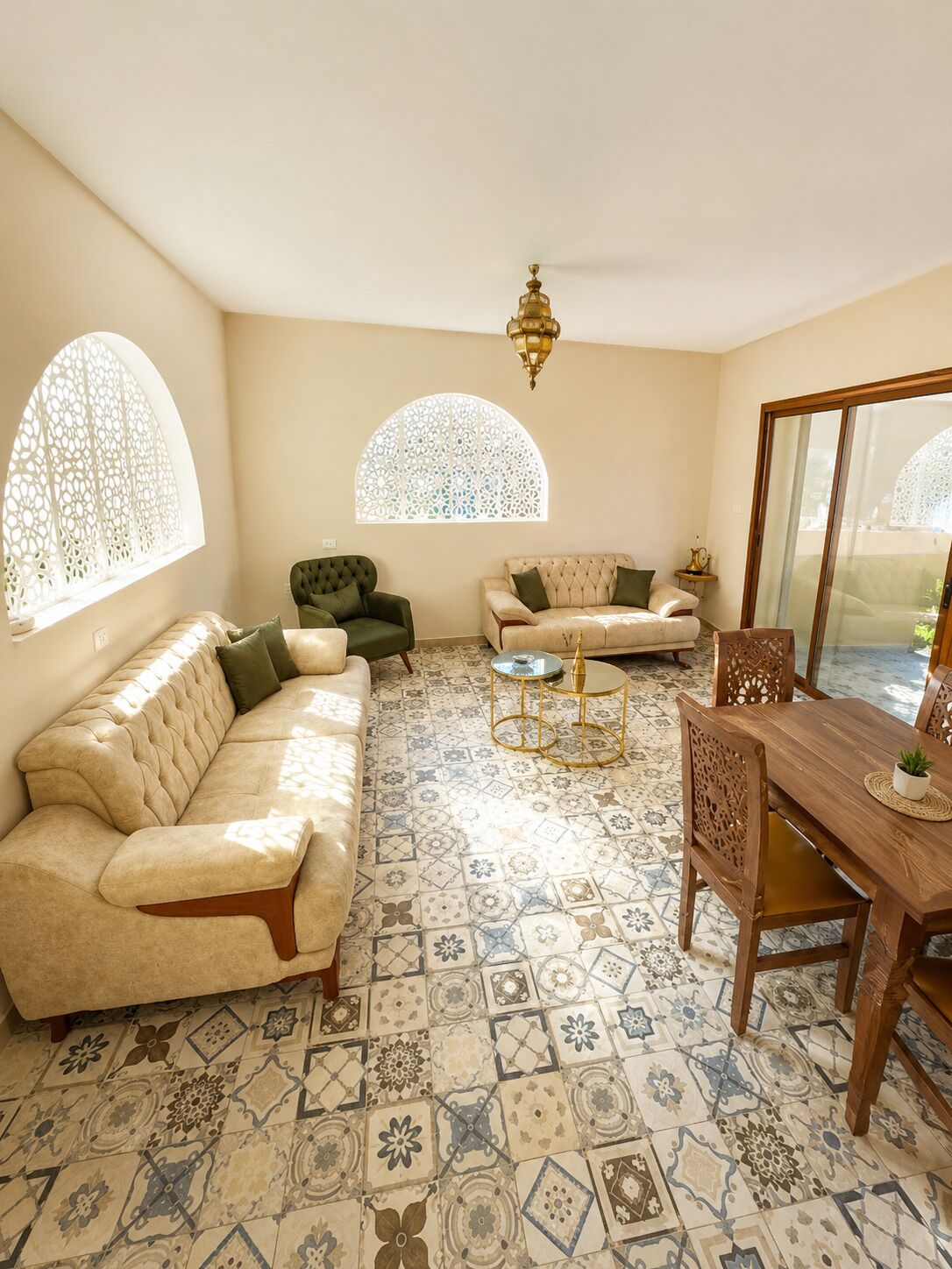 A living room with a beige sofa, a green armchair, a patterned floor, and a dining table with chairs.