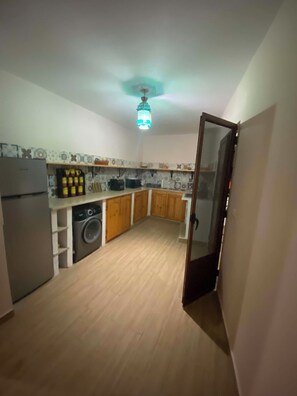 Cocina compacta con armarios de madera, lavadora y refrigerador.