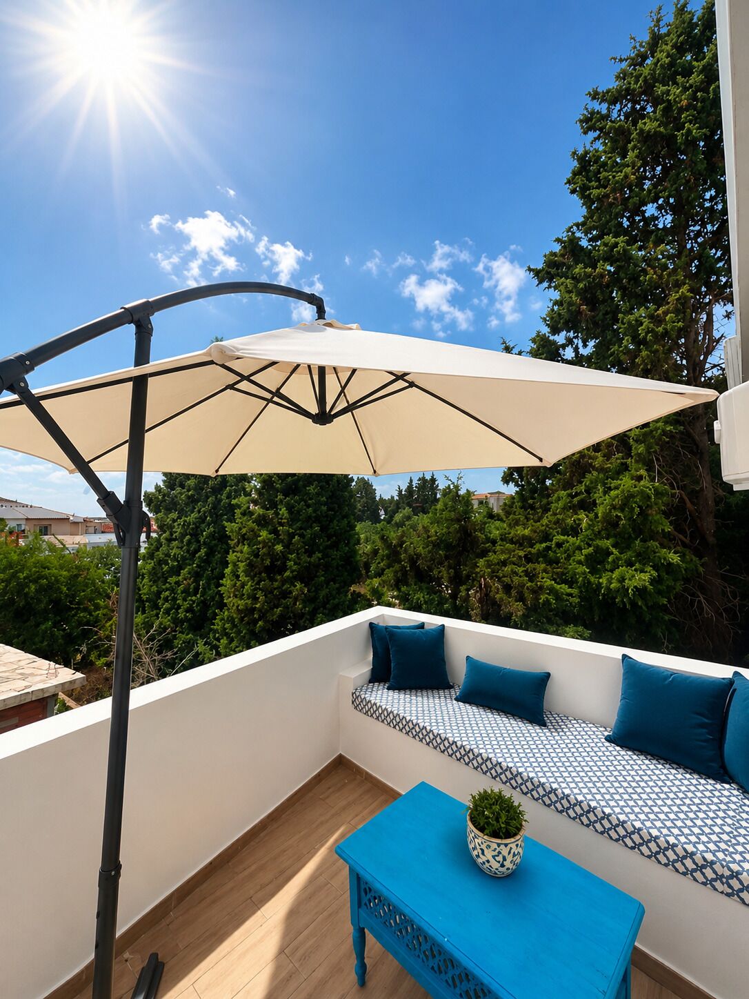 An outdoor seating area with a sun umbrella, a patterned sofa, and a small table with a plant.