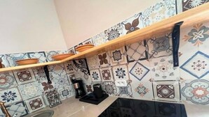 A kitchen with a black stove, a wooden shelf, and patterned tiles. - 2-bedroom apartment in charming Menzel Jemil with AC (Menzel Jemil)