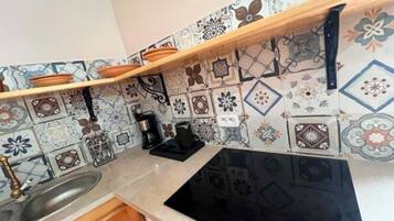 A kitchen with a black stove, a wooden shelf, and patterned tiles.