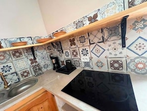 Uma cozinha com fogão preto, prateleira de madeira e ladrilhos estampados.