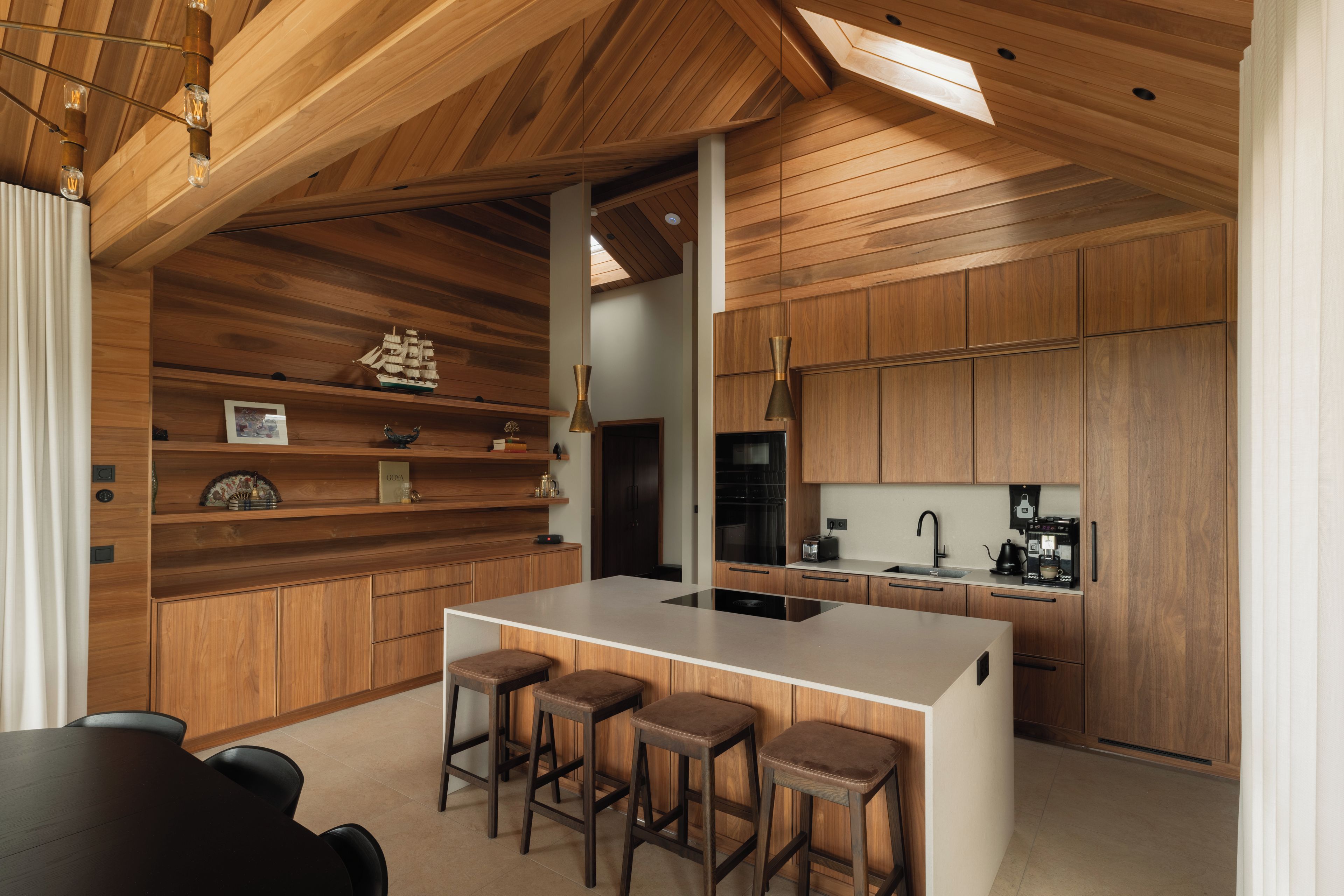 Une cuisine moderne avec des meubles en bois, un îlot central doté de tabourets et un four encastré.