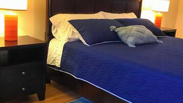 Un lit avec une tête de lit sombre, deux tables de chevet avec des lampes, un tapis à motifs bleus et une fenêtre avec des rideaux.