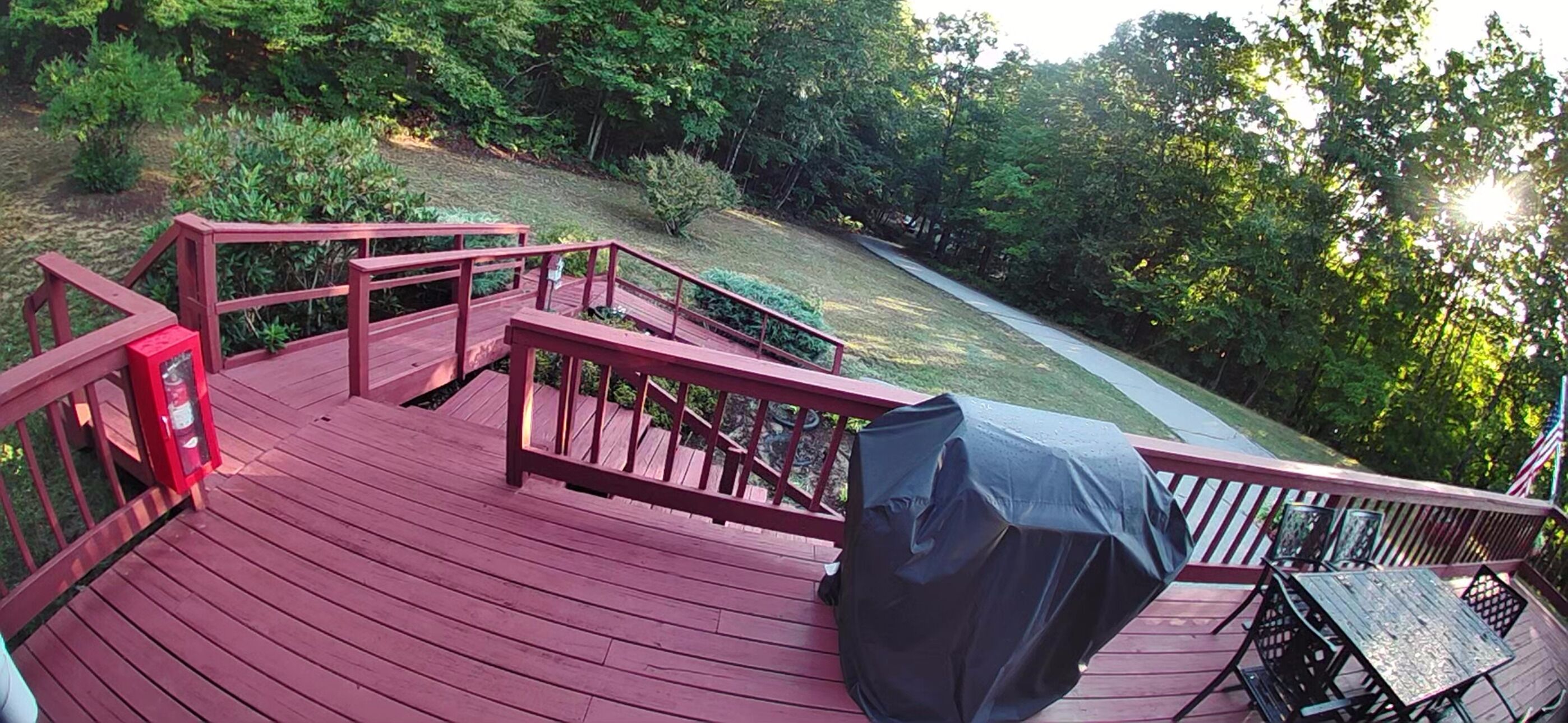 A wooden deck with a covered table and chairs, surrounded by greenery.