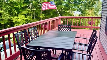 Une terrasse en bois avec une table et des chaises, un drapeau américain et une vue sur les arbres.