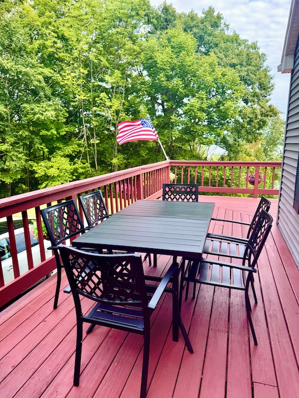 A wooden deck with a table and chairs, an American flag, and a view of trees.