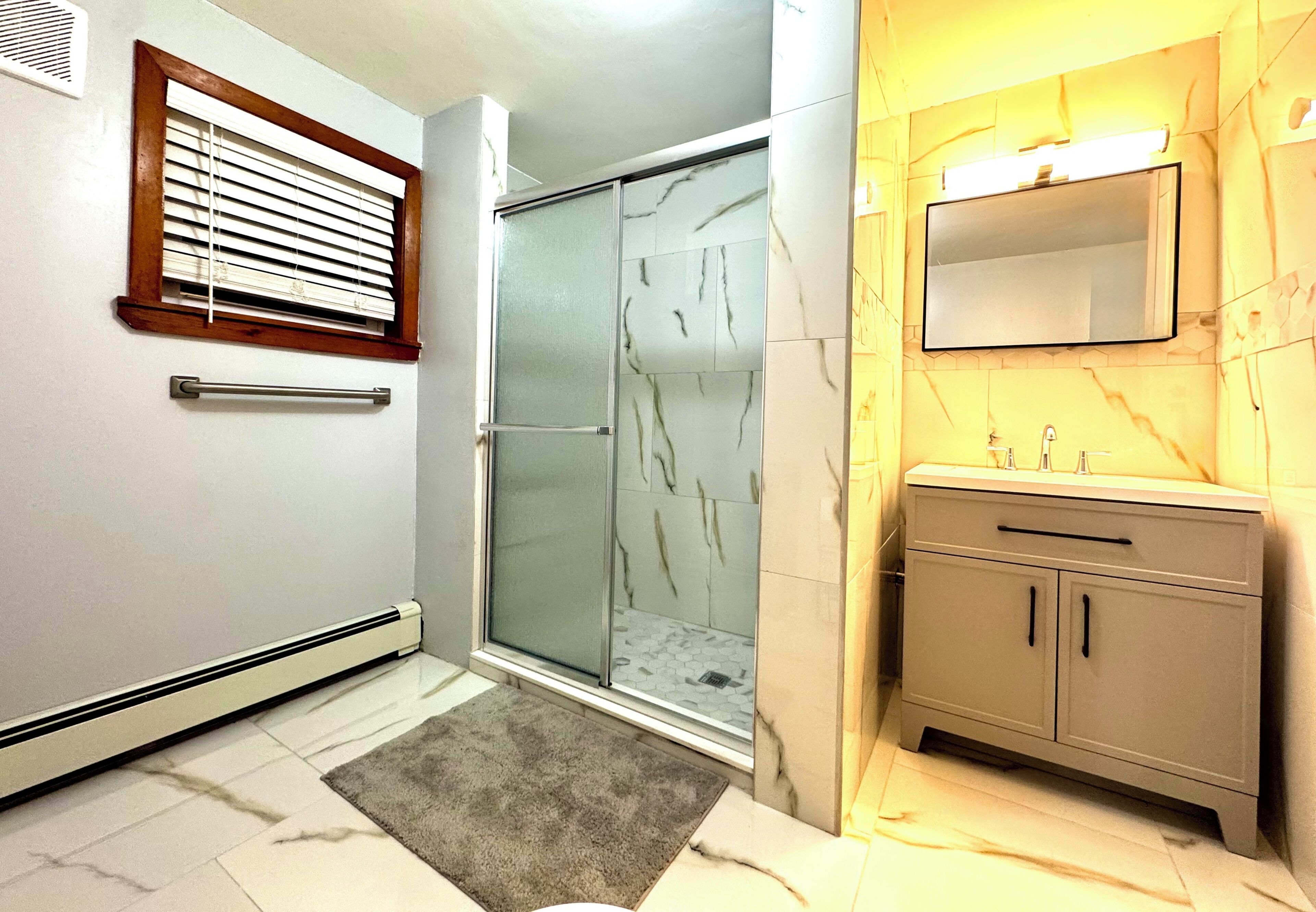 A bathroom with a glass shower enclosure, a vanity with a mirror, and a towel rack.