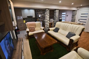 Ein Wohnzimmer mit einer Couch, Sesseln, einem Couchtisch und einem Fernseher.