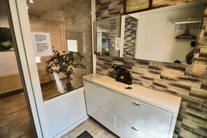 Un bagno con un mobile vanitario bianco, uno specchio, una sveglia e una pianta in vaso.