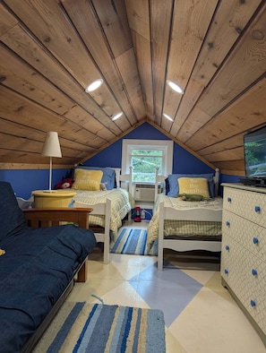A cozy attic bedroom with a sloped ceiling, two beds, a dresser, a lamp, and a television. - Cozy 1-bedroom/ 1 loft cottage in serene Lakeview- sleeps 8 (Lakeview)