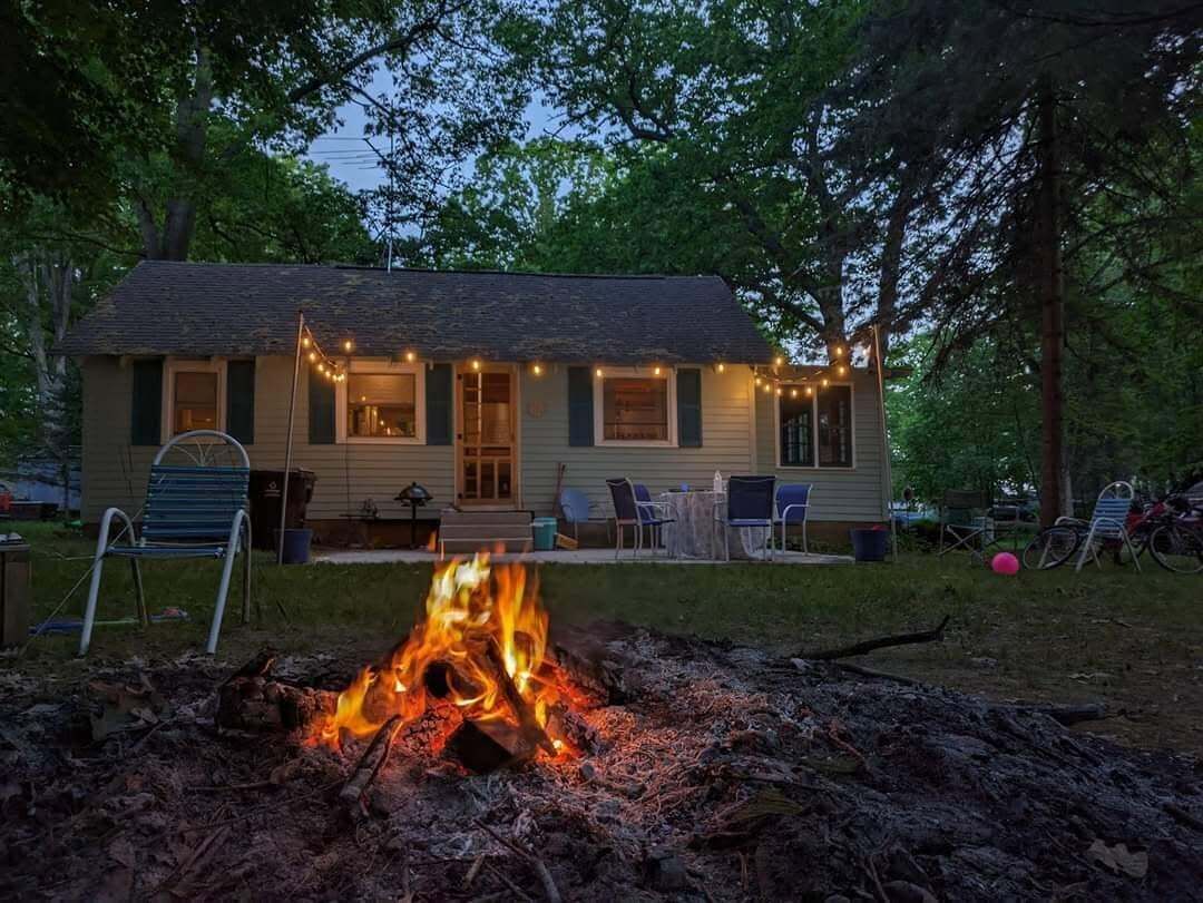 A small house with a fire pit in front, surrounded by trees.