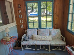 A cozy seating area with a bench and a table, a window with a view of the outdoors, and a wall with the word 'LAUGH' spelled out. - Cozy 1-bedroom/ 1 loft cottage in serene Lakeview- sleeps 8 (Lakeview)