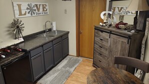 A kitchen with a sink, cabinets, a wooden door, and a decorative sign on the wall.