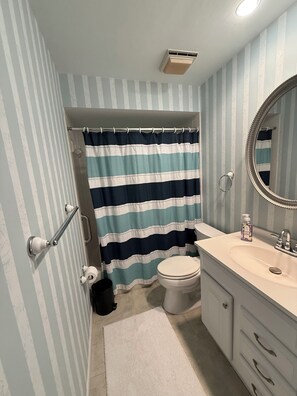 Ein Badezimmer mit gestreiftem Duschvorhang, Toilette, Waschbecken mit Spiegel und Handtuchhalter.