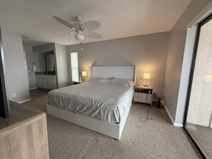 Ein modernes Hotelzimmer mit einem großen Bett, einem Deckenventilator, einem Nachttisch mit Lampe und Blick ins Badezimmer.