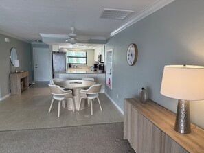 Eine moderne Küche mit einer zentralen Kochinsel, einem Essbereich mit rundem Tisch und einem Wohnbereich mit Lampe und Uhr an der Wand.