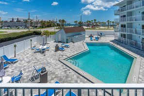 A pool area with a clear blue pool, lounge chairs, and a small building with a door. - NEW! STEPS from the Beach and Pool! Beautiful Ocean View 2nd Floor Studio! (New Smyrna Beach)