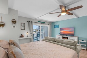 Ein Schlafzimmer mit einem großen Bett, einem Deckenventilator, einem Fernseher und Blick auf den Strand durch eine Schiebetür.