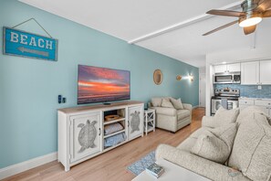Ein Wohnzimmer mit Fernseher, Deckenventilator, Küchenzeile und einem Schild mit der Aufschrift 'BEACH'.