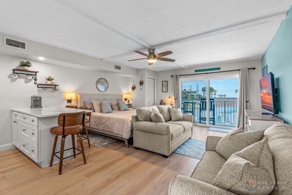 Ein modernes Schlafzimmer mit einem Bett, einem Schreibtisch und einem Stuhl. Ein Balkon bietet Blick aufs Meer.