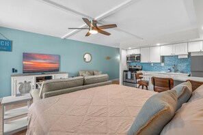 Ein modernes Schlafzimmer mit einem großen Bett, einem Deckenventilator, einem Fernseher und einer Küchenzeile mit Mikrowelle und Herd.
