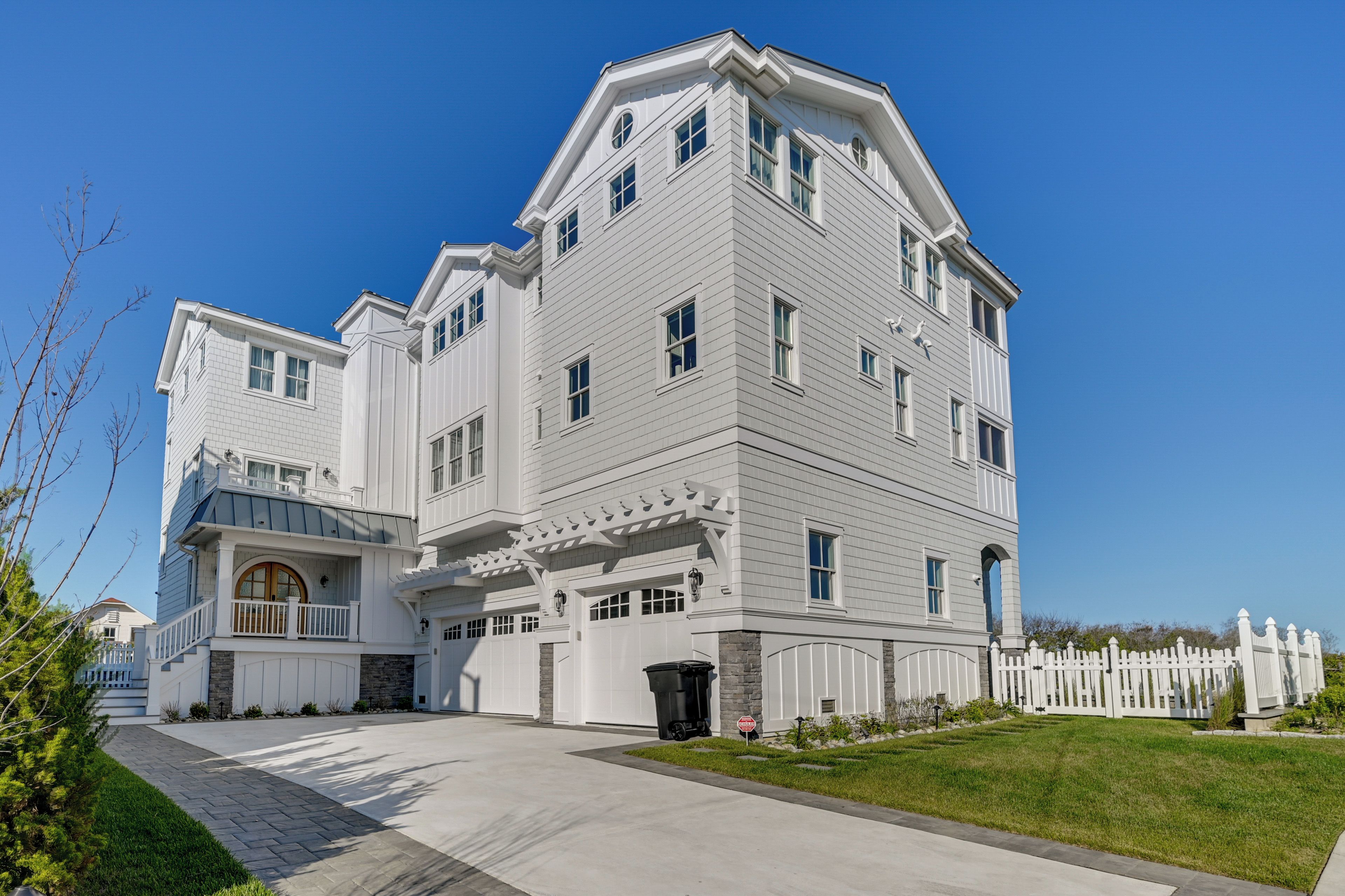 A large, multi-story house with a prominent front porch, a garage, and a white picket fence.