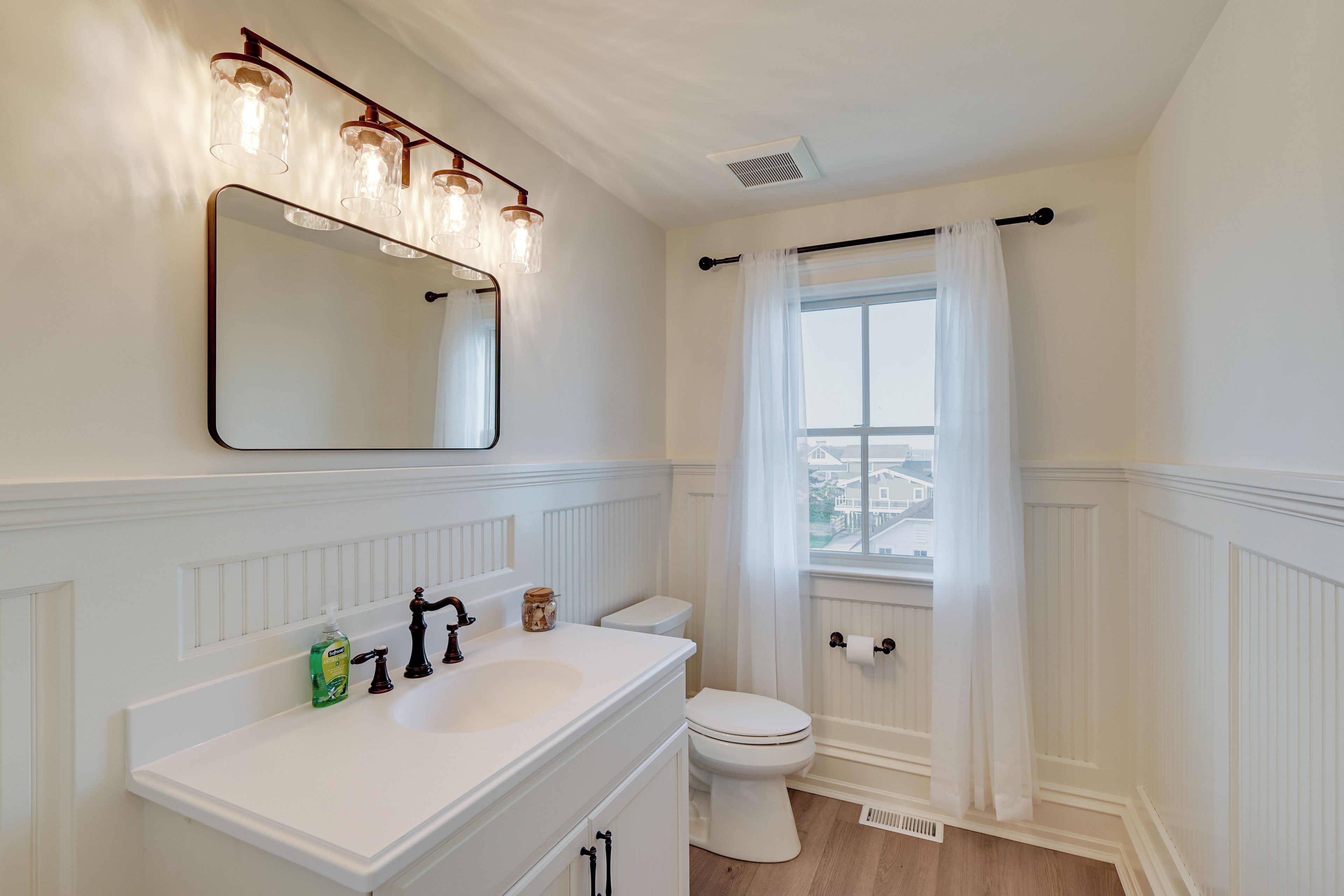 A bathroom with a white vanity, a mirror, a toilet, and a window with a view of buildings outside.