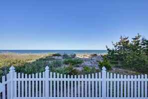 Ein weißer Zaun, ein Sandstrand und Meerblick.