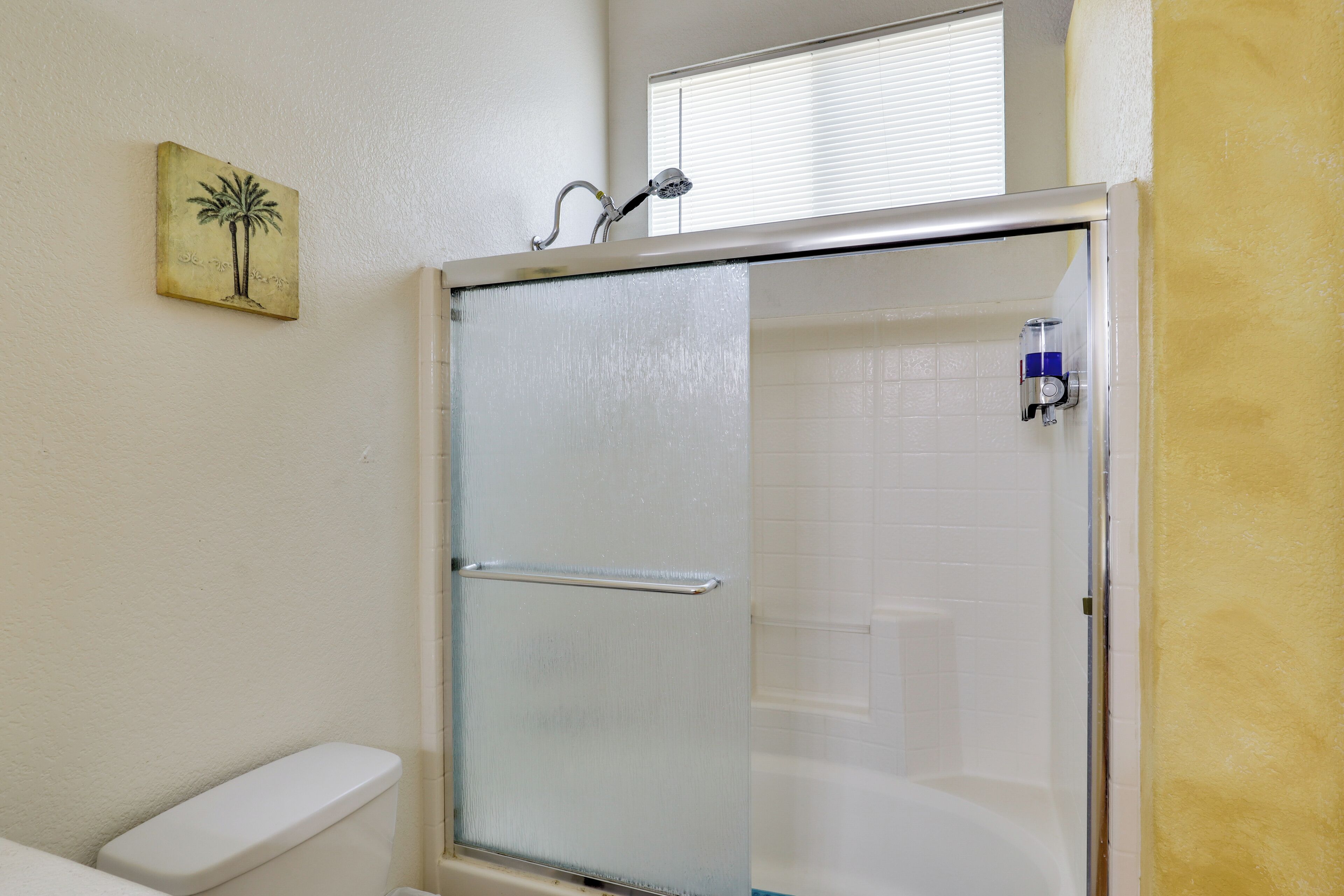 A bathroom with a glass-enclosed shower, a toilet, and a wall-mounted soap dispenser.