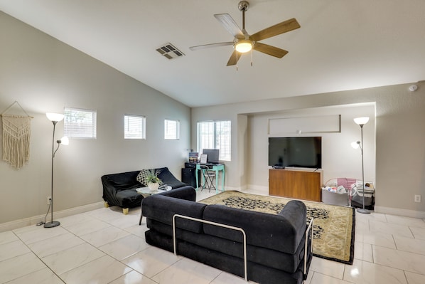A modern living room with a ceiling fan, a flat-screen TV, a black sofa, a coffee table, and a patterned rug.