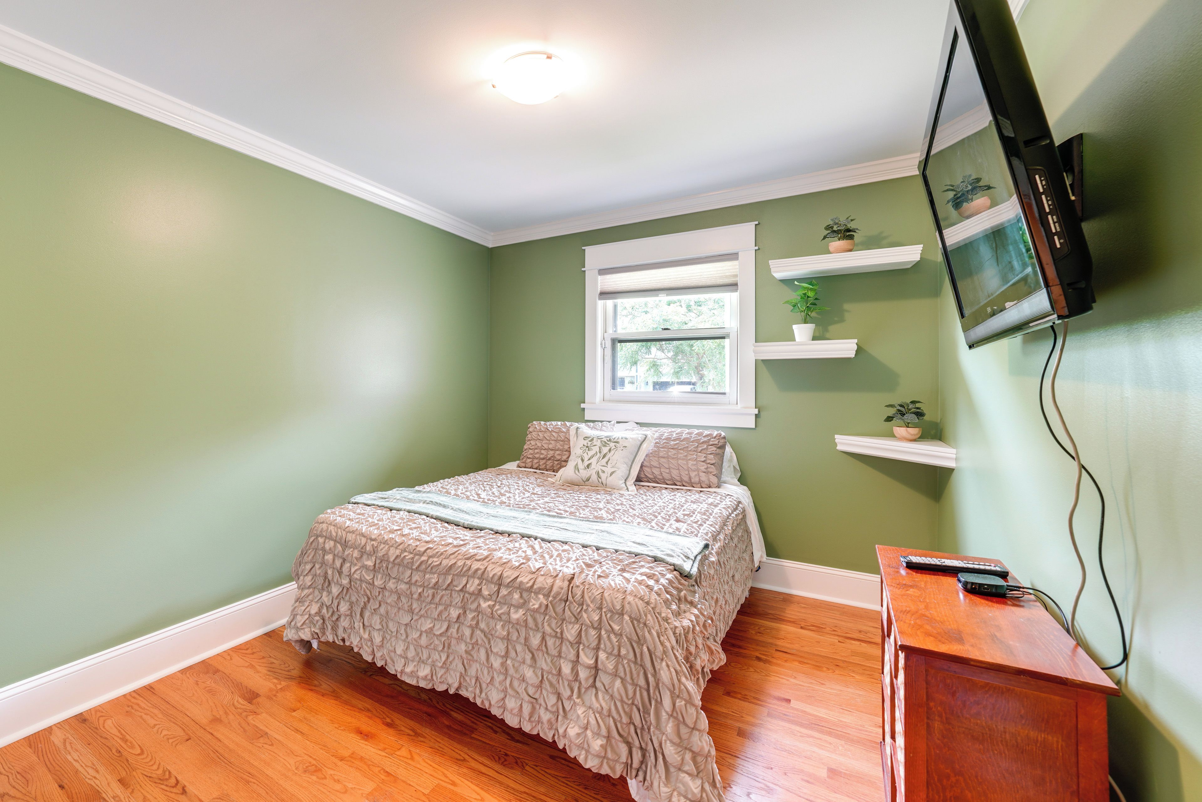 A bedroom with a bed, a television mounted on the wall, and a window with blinds.