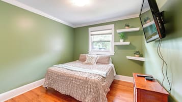 A bedroom with a bed, a television mounted on the wall, and a window with blinds.