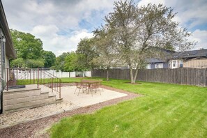 A backyard with a patio, a wooden fence, and a large tree.
