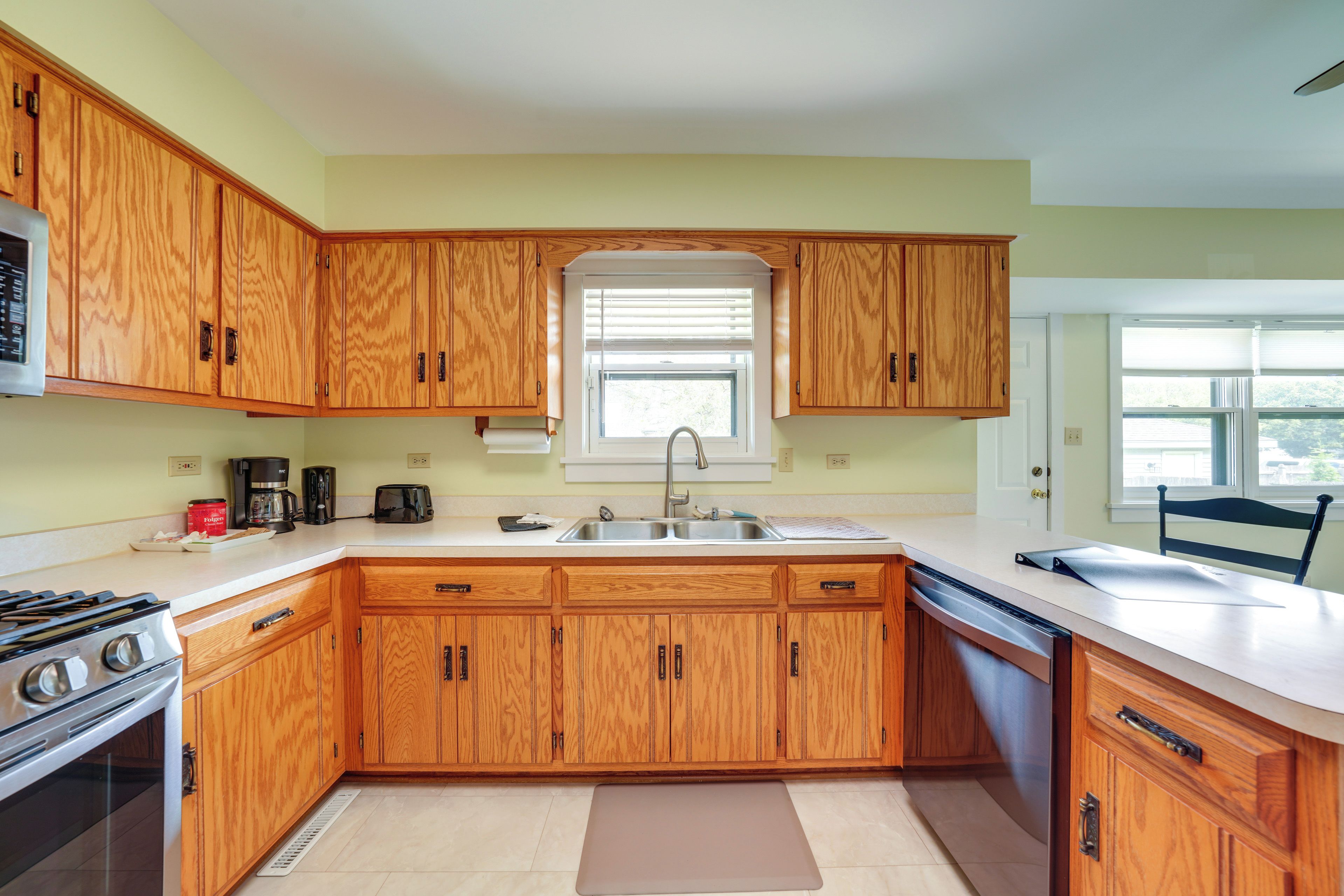 A kitchen with wooden cabinets, a gas stove, a dishwasher, and a window with blinds.