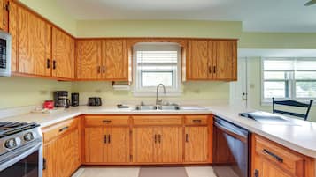 A kitchen with wooden cabinets, a gas stove, a dishwasher, and a window with blinds.