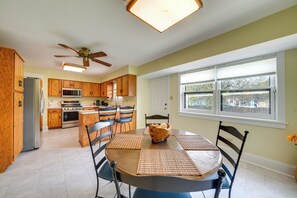 A modern kitchen with wooden cabinets, a central island, and a dining area with a round table and chairs.