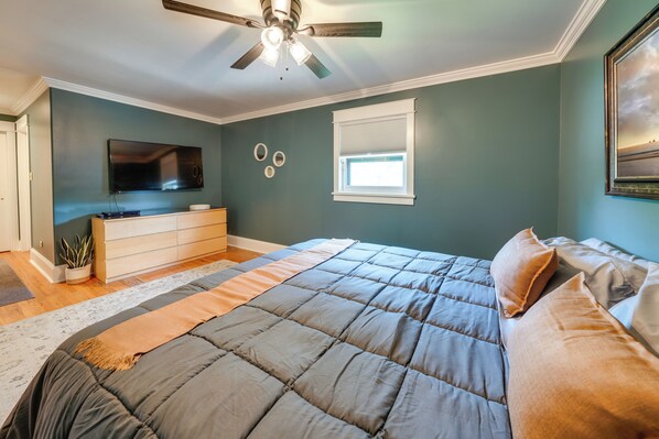 A bedroom with a bed, a ceiling fan, a TV, a window, and a dresser.