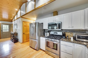 A modern kitchen with stainless steel appliances, white cabinetry, and a wooden ceiling.